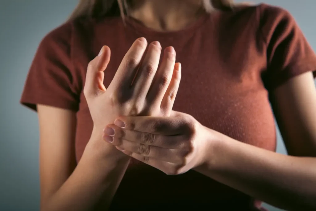 Femme en t-shirt qui se tient le poignet d'une main, paume ouverte